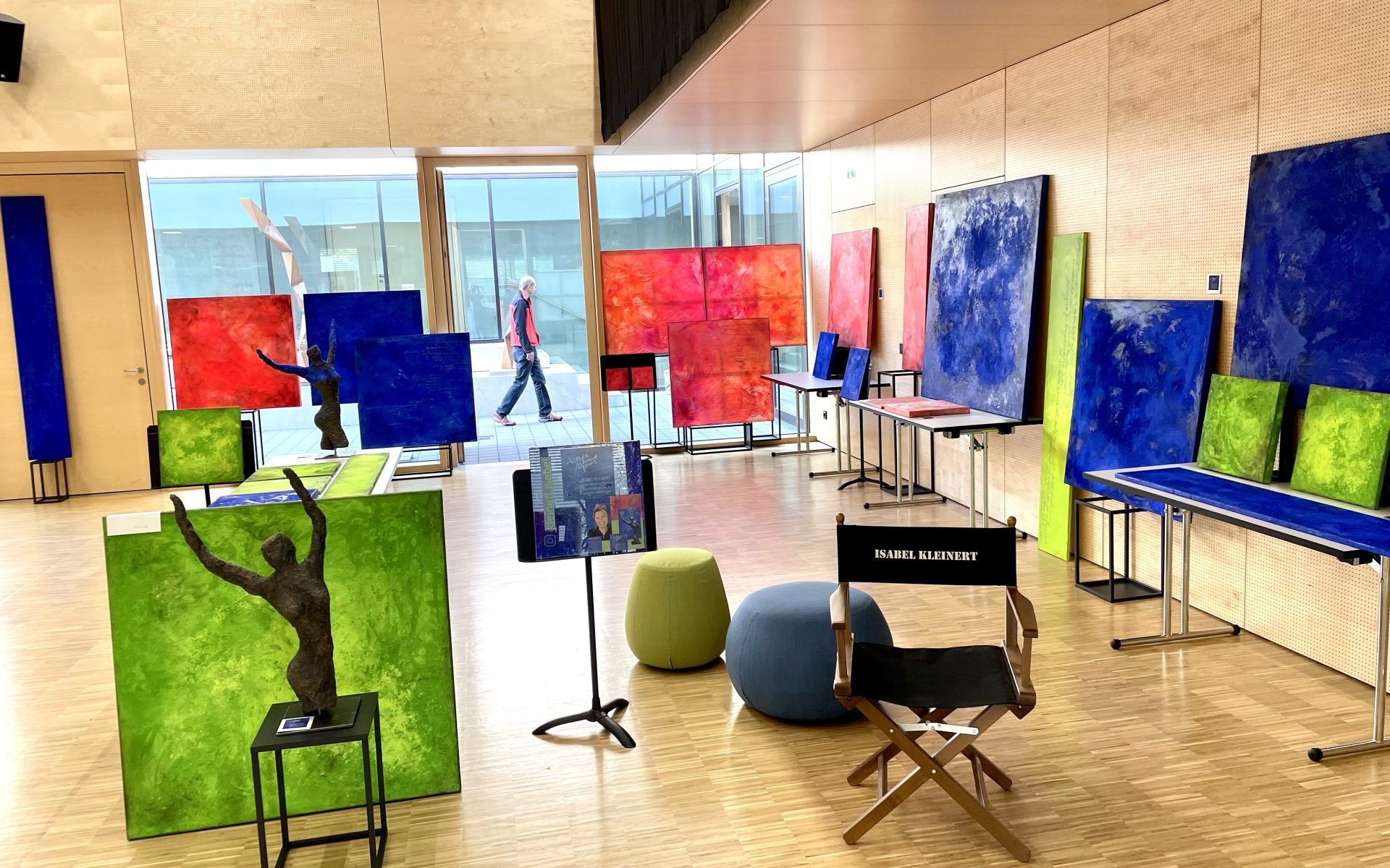 Art exhibition room with colorful abstract paintings, sculptures, and a director’s chair labeled “Isabel Kleinert.”