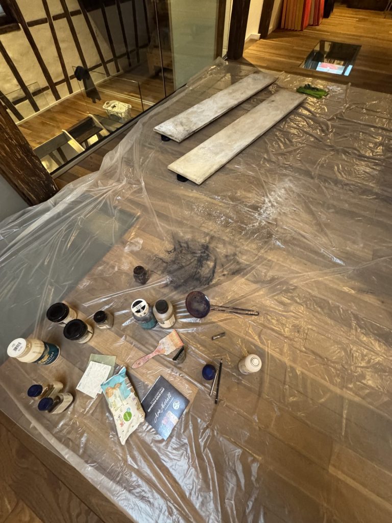 Nahaufnahme eines Holzbodens mit verstreuten Werkzeugen, Farbdosen und Renovierungsmaterialien.