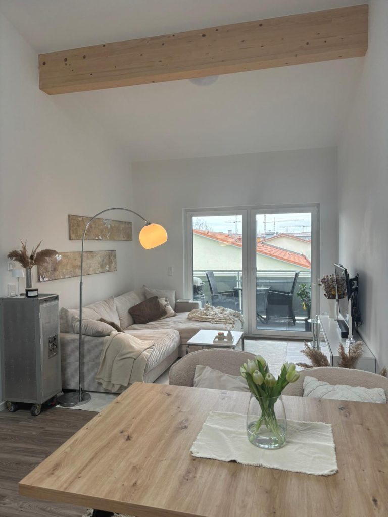 Helles, modern eingerichtetes Wohnzimmer mit Sofa, Couchtisch und Balkonzugang.